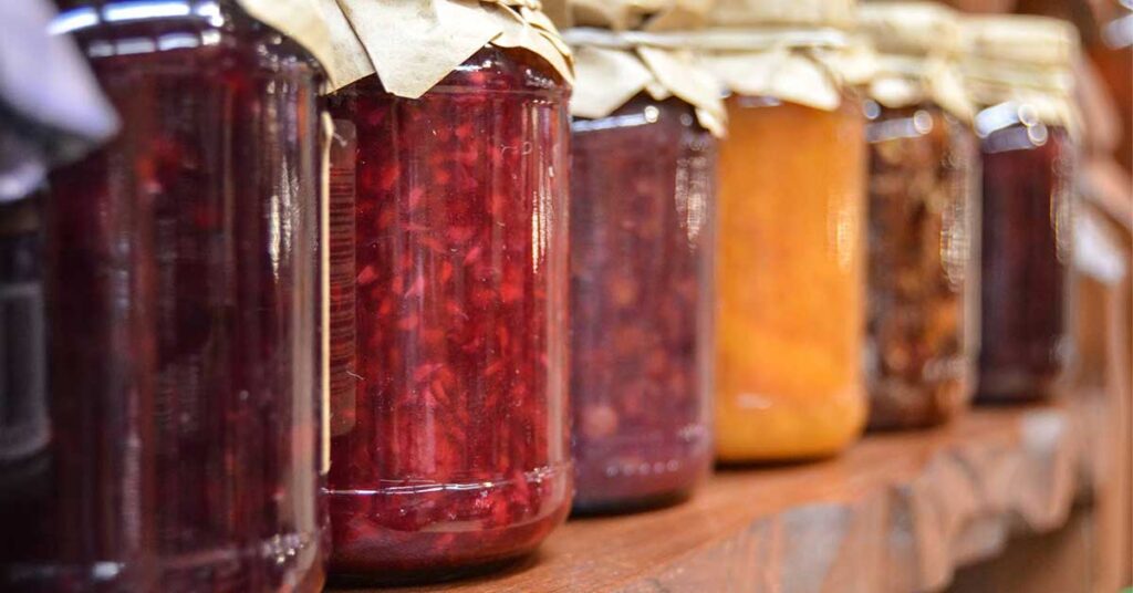 Jars of canned jellies and jams on a wooden shelf